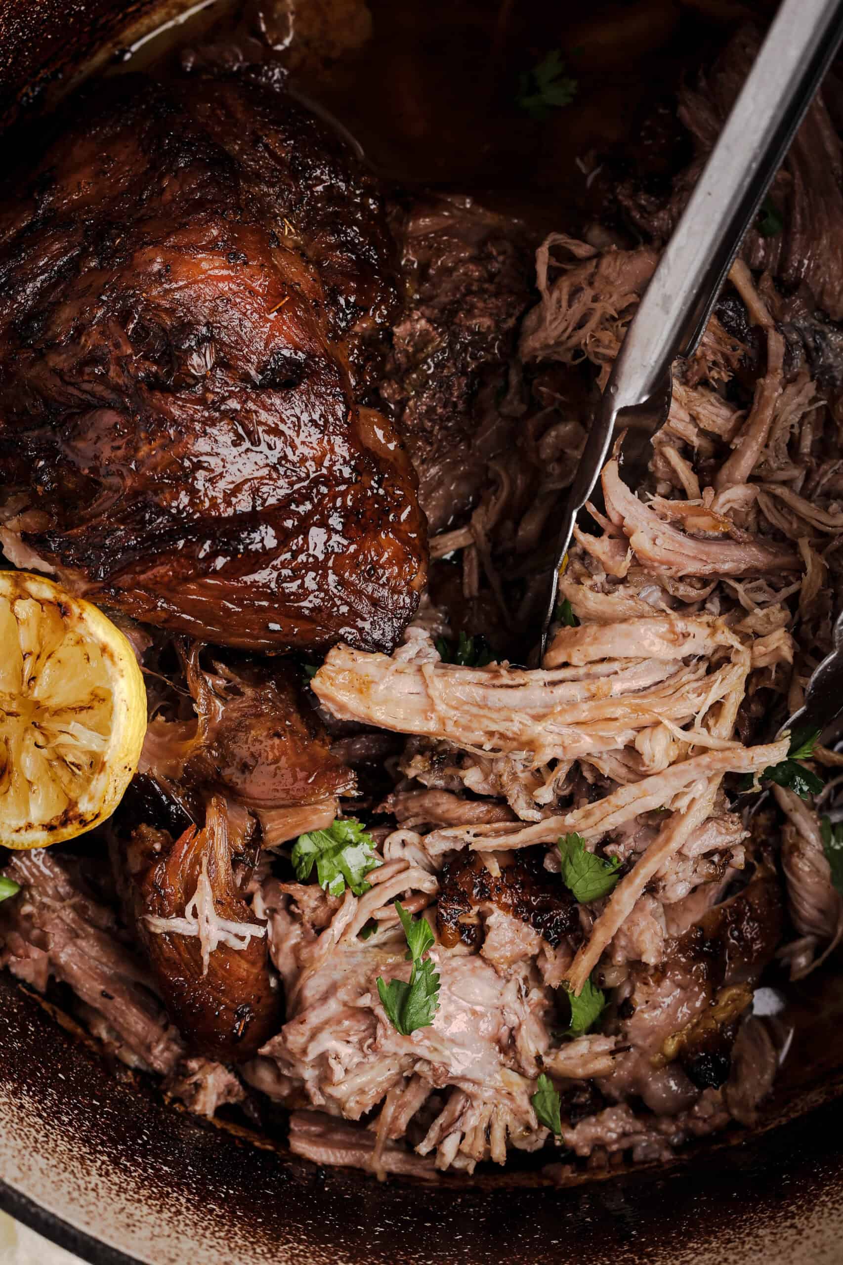 Tender shredded mojo pork roast with crispy caramelized pieces served in a Dutch oven with roasted citrus and cooking juices.