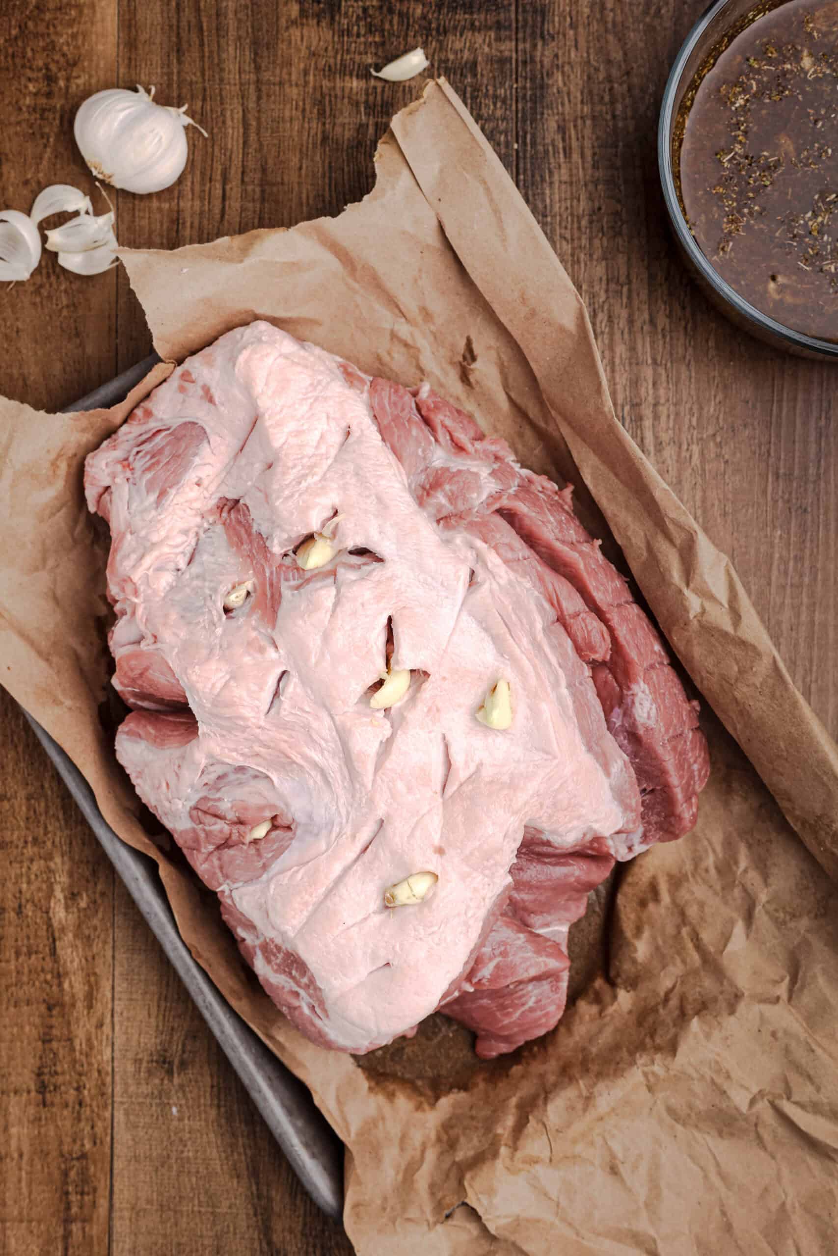 Pork shoulder prepared for mojo roast with garlic cloves inserted into slits cut throughout the meat.
