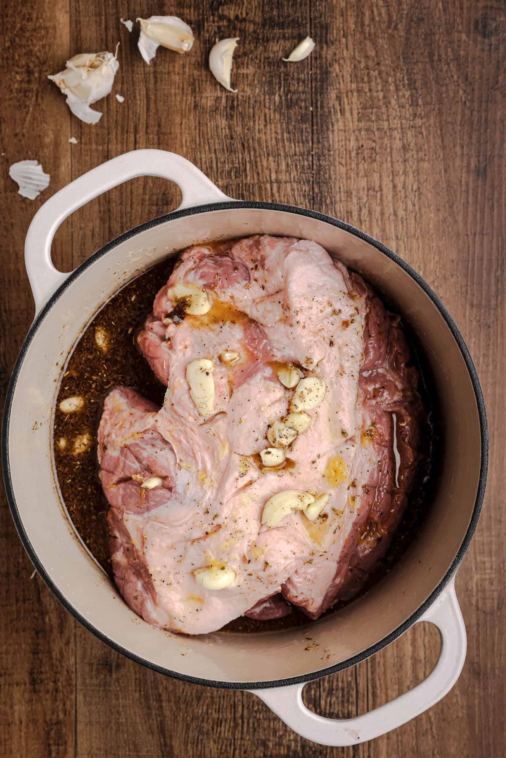Pork shoulder marinating in citrus-garlic mojo sauce inside a Dutch oven before roasting.