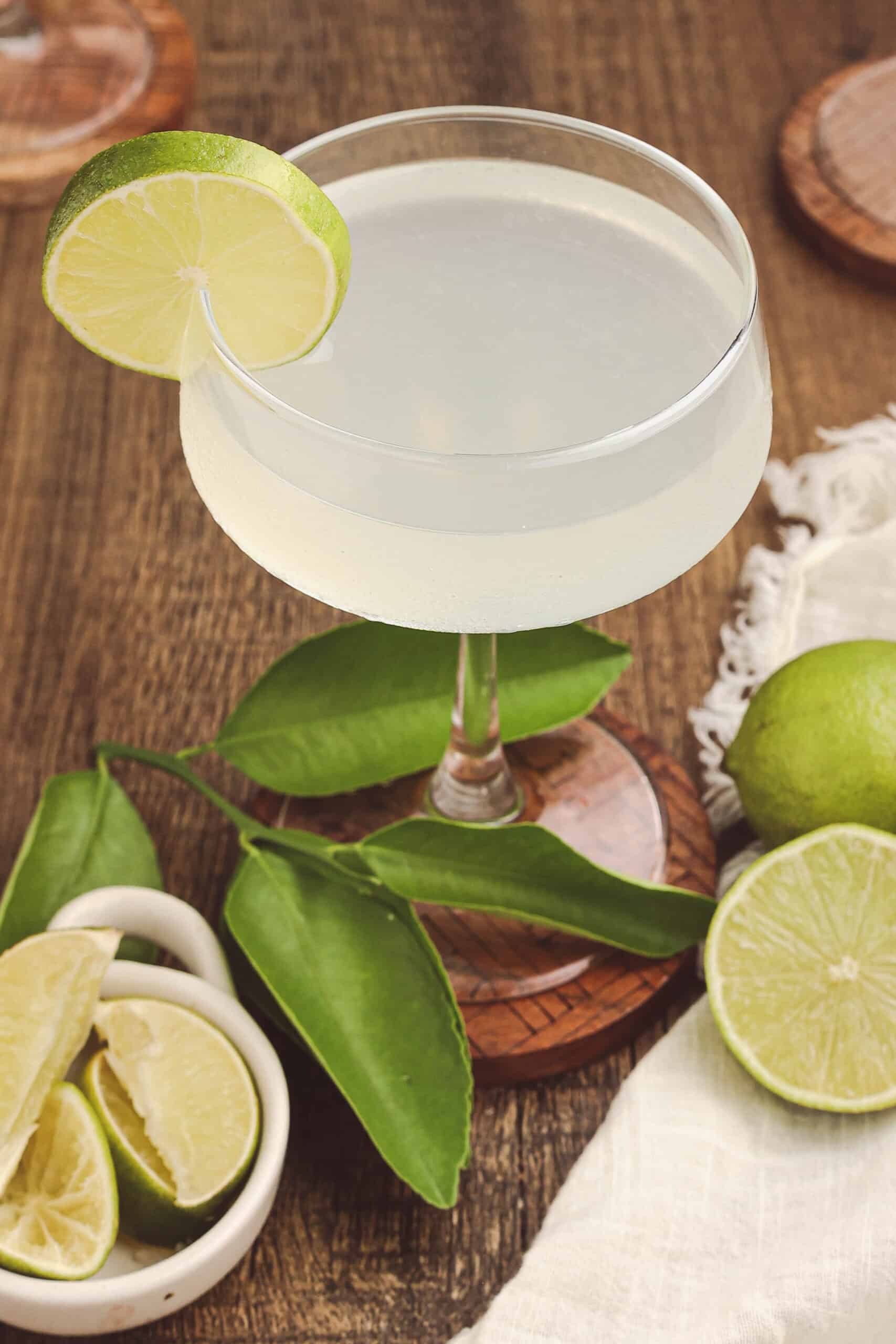 Classic daiquiri cocktail photographed from above with fresh limes, citrus leaves, and a vintage wooden tabletop.