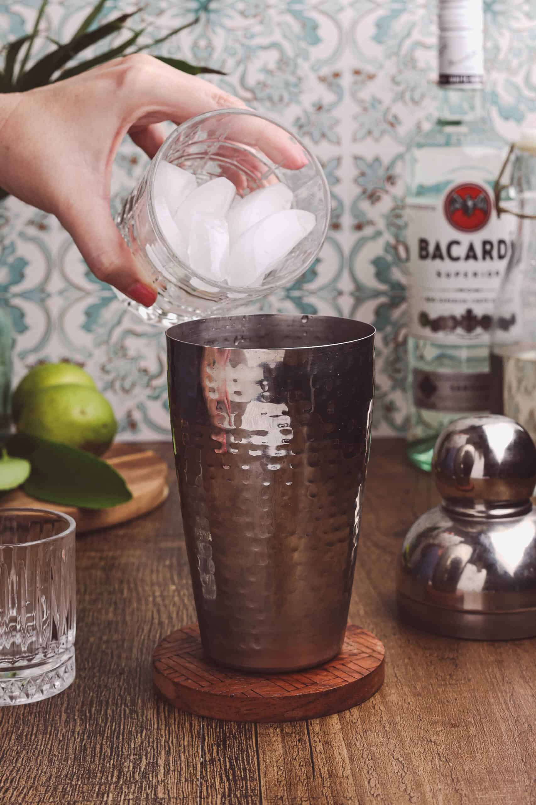 Adding ice cubes to a cocktail shaker to prepare a classic daiquiri.