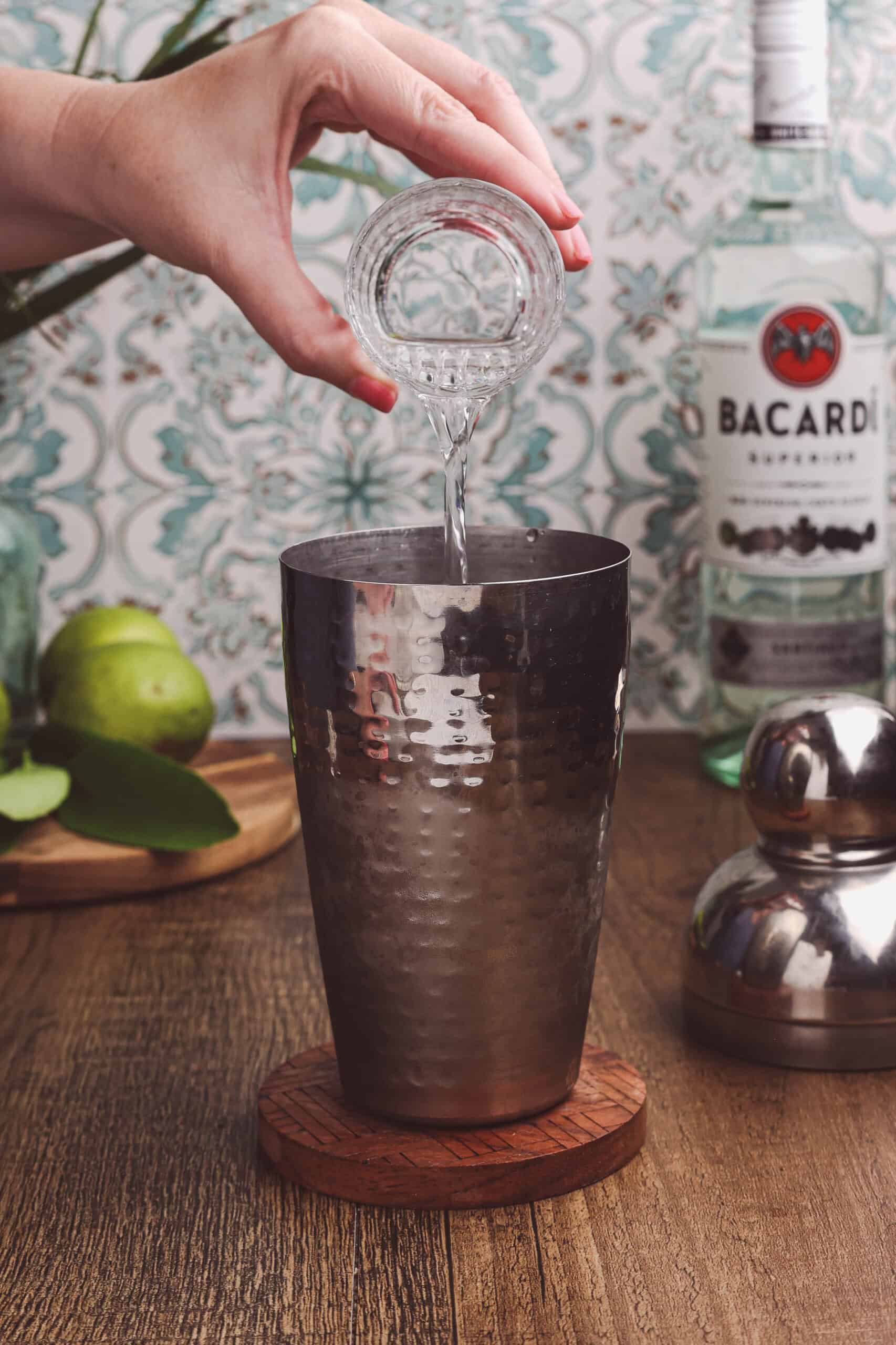 Pouring simple syrup into a cocktail shaker for a classic daiquiri recipe.