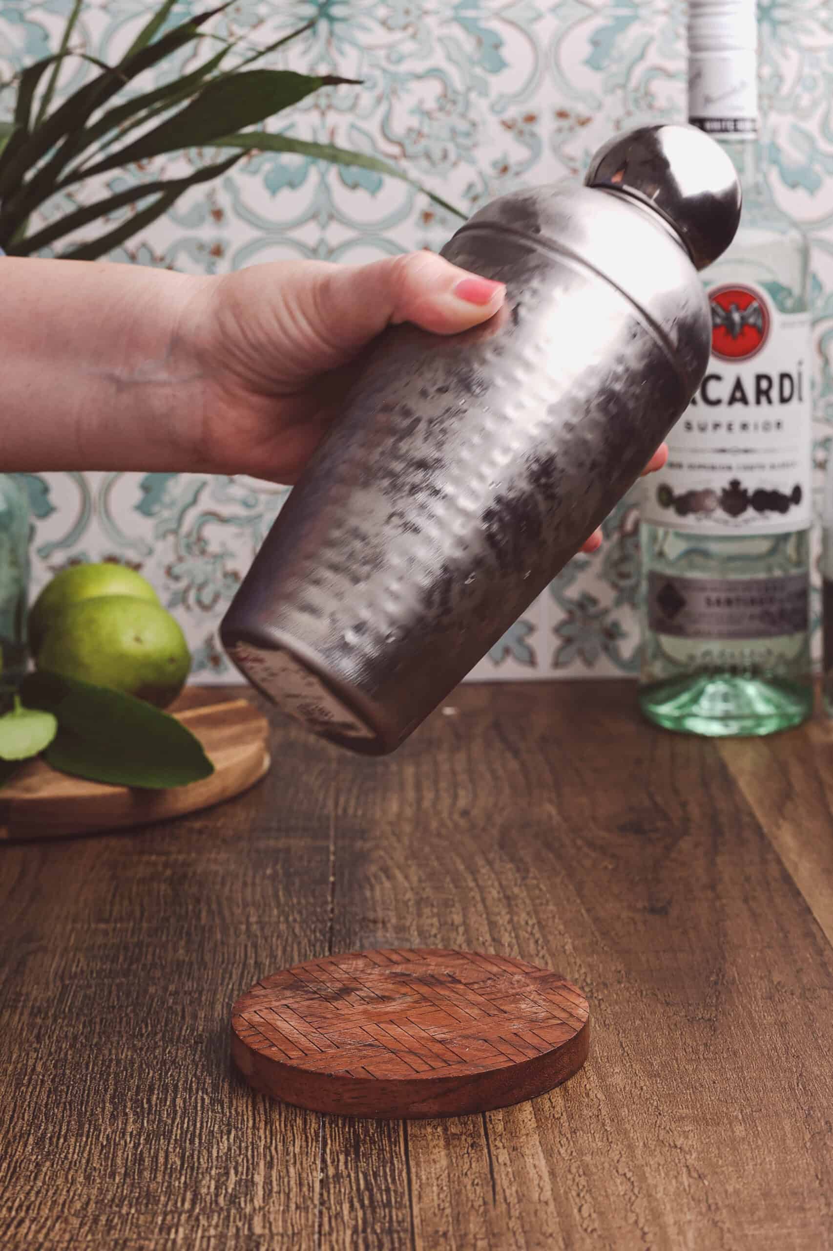 Shaking a cocktail shaker filled with rum, lime juice, simple syrup, and ice for a classic daiquiri.