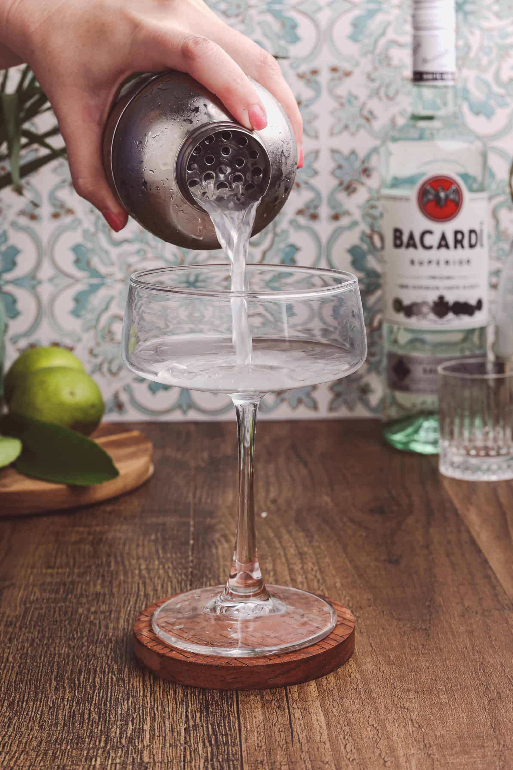 Straining a freshly shaken classic daiquiri into a chilled coupe glass.