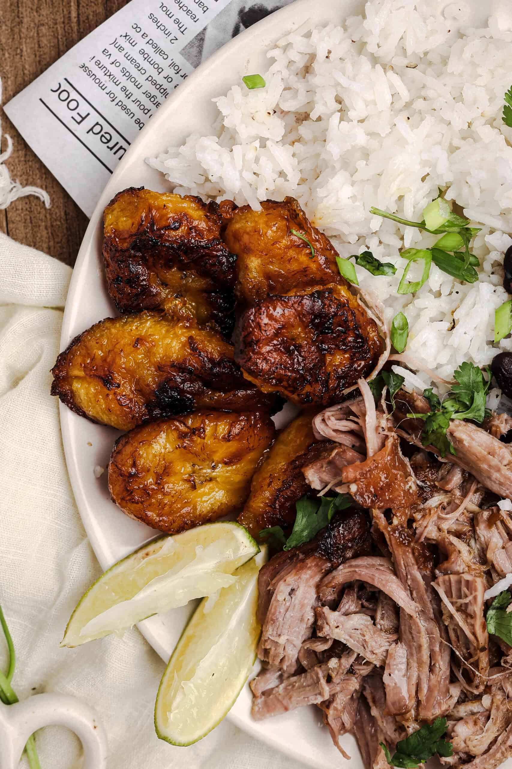 Fried sweet plantains served alongside mojo pork, white rice, black beans, and lime wedges on a Cuban-inspired dinner plate.