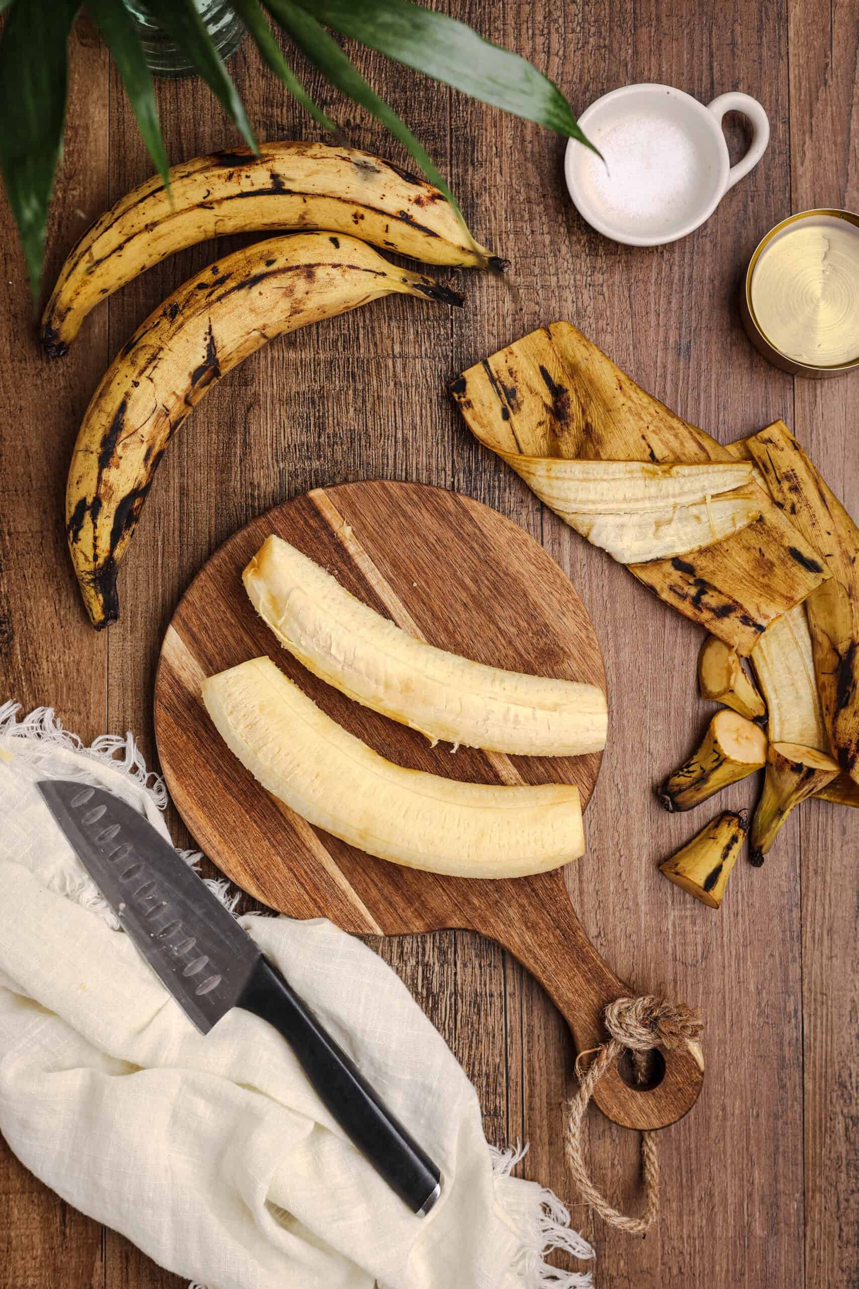 Peeled ripe plantains on a wooden cutting board with plantain peels and a chef’s knife, preparing ingredients for fried sweet plantains.